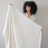 Woman stands holding a floral minky stretch blanket with a warm neutral floral print on it. 