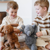 Two little boys each hold a stuffed animal from Saranoni. One little boy is holding a brown dog stuffed animal and the other little boy is holding a gray elephant stuffed animal.