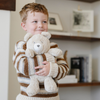 A little boy hugs a light tan bear stuffed animal. The bear stuffed animal is from Saranoni. 