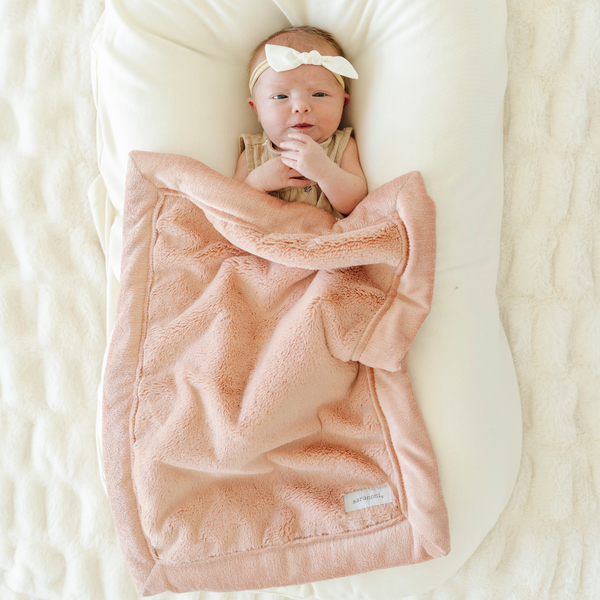 Baby girl snuggled with Saranoni soft Lush Mini baby blanket in Blossom color. 