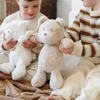 A little boy holds a light tan bear stuffed animal. The bear stuffed animal is from Saranoni. Another little boy holds a white lamb stuffed animal that is also from Saranoni.