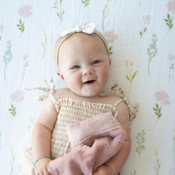 Baby girl snuggled with Saranoni baby blanket while laying on Floral Fields Cotton Muslin crib sheet. 