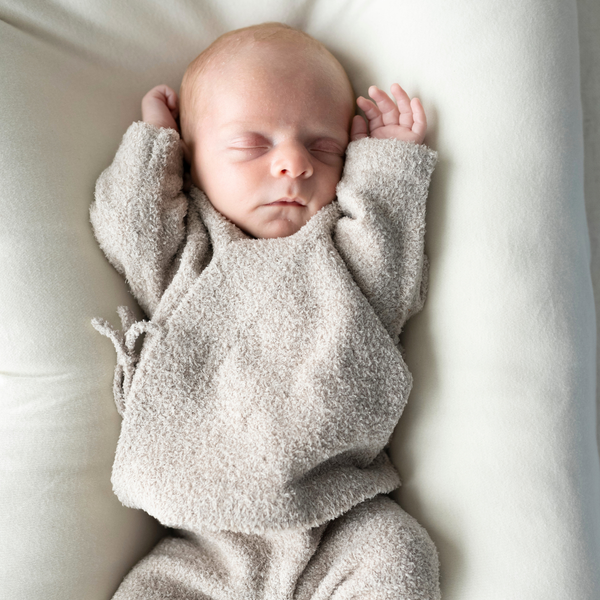 Newborn baby wrapped in a soft, beige blanket on a white surface