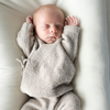 Newborn baby wrapped in a soft, beige blanket on a white surface