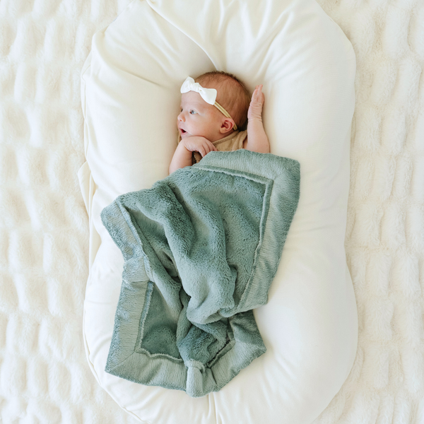 Baby girl snuggled with Eucalyptus Lush Mini soft baby blanket. 