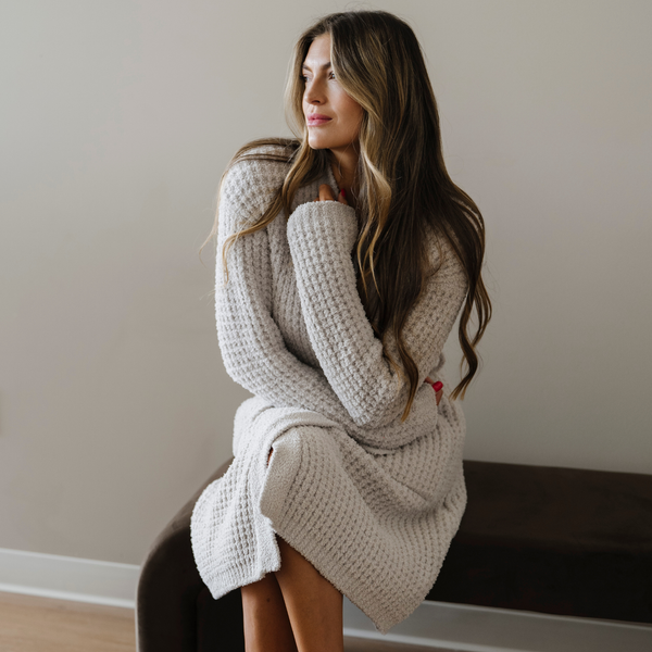 Woman sitting, wearing a moonbeam light gray waffle knit robe. 