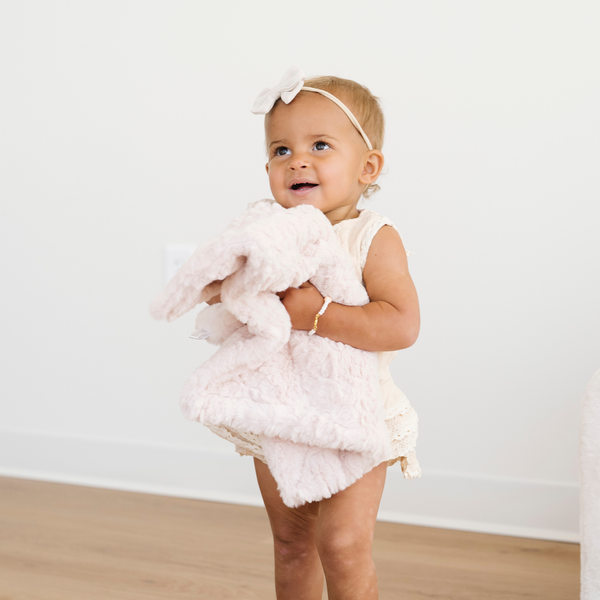 Toddler girl holding a blush pink dream faux fur mini baby blanket. 