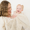 Mom holding baby girl snuggled with Dream faux fur receiving blanket in Oat.