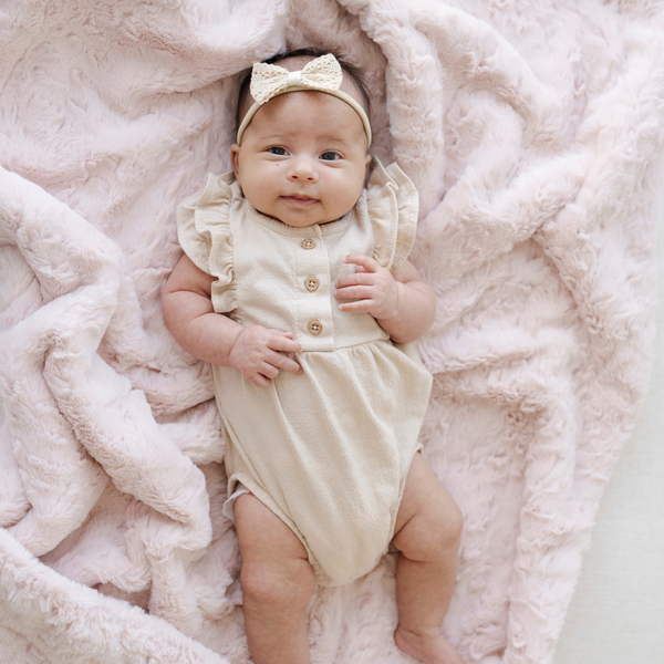 Baby girl laying on top of a blush pink dream faux fur receiving baby blanket. 