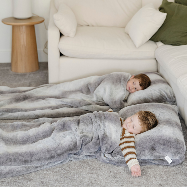 Two little boys each lay in their own faux fur sleeping bag. The sleeping bags are from Saranoni and are a light grey blended with dark gray color.