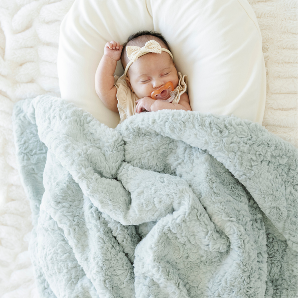 Baby girl sleeping with a mint green dream faux fur receiving blanket next to her. 