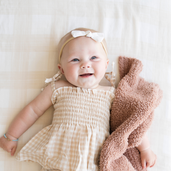 Baby girl laying on Perfectly Plaid Cotton Muslin Crib Sheet snuggled with baby blanket.