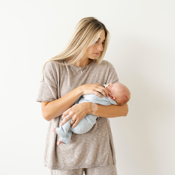 Woman holding a newborn baby wearing a light blue bamboni lite outfit. 