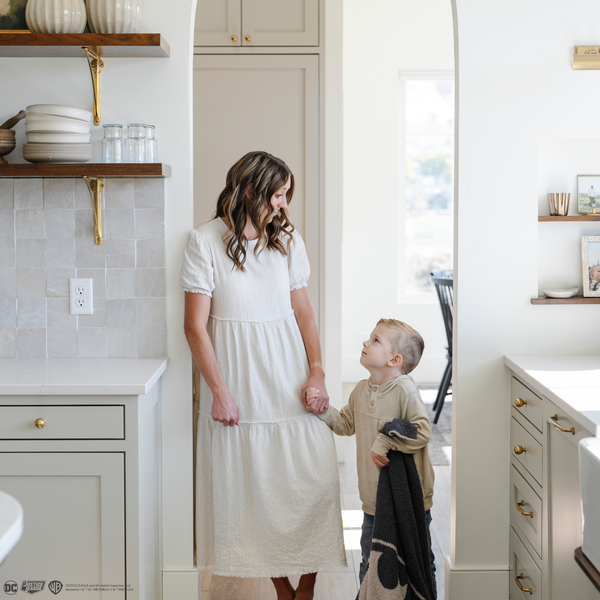 A little boy stands by his mom while holding a black and light gray double-layer Bamboni® blanket with a Batman™ icon on it. The soft blanket is a luxury blanket and a kids blanket as well as a Saranoni blanket. This kids blanket is perfect for littles. 