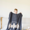 A little boy holds a black and light gray double-layer Bamboni® blanket with a Batman™ icon on it. The soft blanket is a luxury blanket and a receiving blanket as well as a Saranoni blanket. This kids blanket is perfect for littles. 