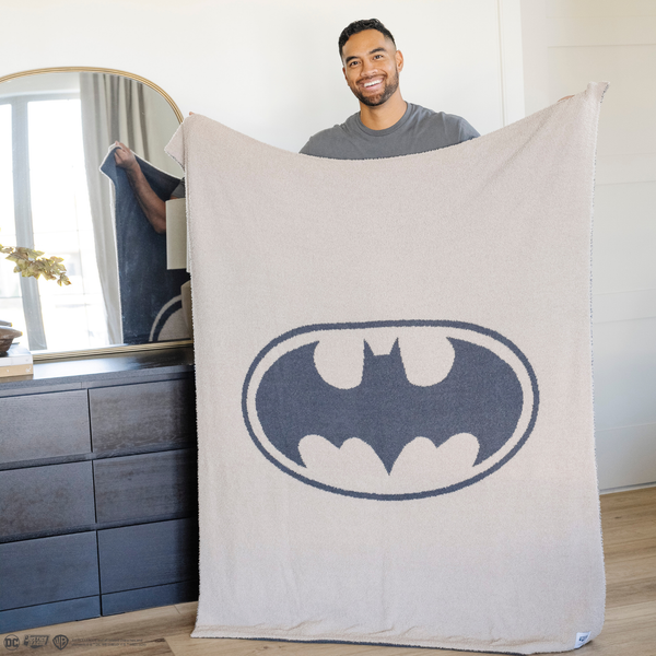 A man holds a black and light gray double-layer Bamboni® blanket with a Batman™ icon on it. The soft blanket is a luxury blanket and a throw blanket as well as a Saranoni blanket. 