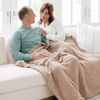 A husband and wife sit with a Bamboni® blanket by Saranoni. This ultra-soft blanket is a light brown blanket and made from a premium blend of bamboo rayon and poly microfiber, offering a lightweight, breathable, and fluffy feel. Perfect as a extra large blanket, luxury blanket, or soft blanket, it adds warmth and elegance to any living room, bedroom, or home décor setting. Designed for ultimate comfort, this buttery-soft Saranoni blanket is ideal for gifting. Enjoy this cozy blanket for years to come!