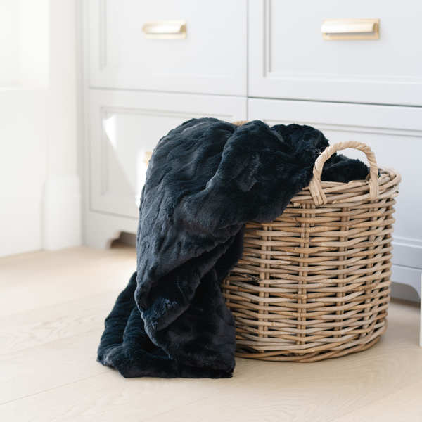 A black luxurious patterned faux fur throw blanket that is a Saranoni blanket is partly in a basket. This ultra-soft, plush throw blanket adds a touch of elegance and warmth to any space, perfect as a soft throw blanket or fluffy blanket for lounging. Ideal for those seeking a high-quality artificial fur blanket or luxury blanket, this versatile and stylish soft blanket enhances both comfort and decor. Shop the best blankets and throws for ultimate relaxation and cozy vibes.