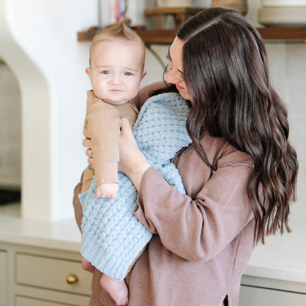 A mother holds her baby boy and a buttery-soft Saranoni blanket, featuring a breathable, plush waffle texture in a soothing blue hue. This luxury mini blanket is the best baby blanket as a newborn blanket and infant blanket—perfect as a cozy blanket for snuggles or a must-have infant blanket. Designed for softness and comfort, this plush baby blanket makes an ideal baby boy gift or gift for new moms. Enjoy this luxury blanket!