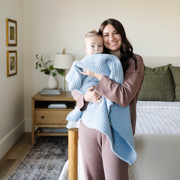 A mother smiles and has her little boy wrapped in a buttery-soft Saranoni blanket, featuring a breathable, plush waffle texture in a soothing blue hue. This luxury receiving blanket is the best baby blanket as a  newborn blanket, infant blanket, baby blanket, or toddler blanket—perfect as a cozy blanket for snuggles or a must-have infant blanket. Designed for softness and comfort, this plush baby blanket makes an ideal baby gift or gift for new moms. Enjoy this luxury blanket!