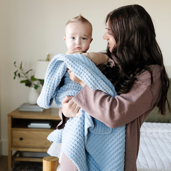 A mother holds her little boy in a buttery-soft Saranoni blanket, featuring a breathable, plush waffle texture in a soothing blue hue. This luxury receiving blanket is the best baby blanket as a  newborn blanket, infant blanket, baby blanket, or toddler blanket—perfect as a cozy blanket for snuggles or a must-have infant blanket. Designed for softness and comfort, this plush baby blanket makes an ideal baby gift or gift for new moms. Enjoy this luxury blanket!