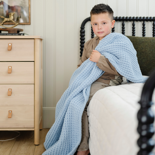 A little boy holds a buttery-soft Saranoni blanket, featuring a breathable, plush waffle texture in a soothing blue hue. This luxury toddler blanket is the best kids blanket as a baby blanket or toddler blanket—perfect as a cozy blanket for snuggles or a must-have infant blanket. Designed for softness and comfort, this plush toddler blanket makes an ideal toddler gift. Enjoy this luxury blanket!