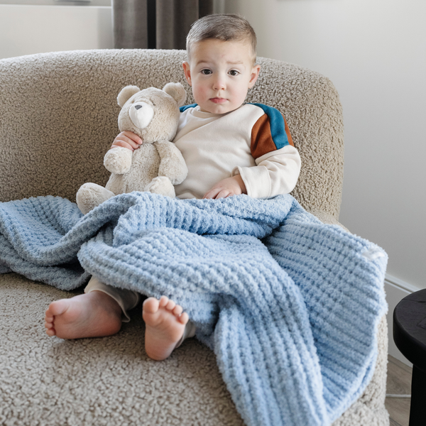 A little boy sits with a buttery-soft Saranoni blanket, featuring a breathable, plush waffle texture in a soothing blue hue. This luxury toddler blanket is the best kids blanket as a baby blanket or toddler blanket—perfect as a cozy blanket for snuggles or a must-have infant blanket. Designed for softness and comfort, this plush toddler blanket makes an ideal toddler gift. Enjoy this luxury blanket!