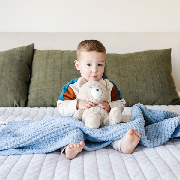 A little boy sits with a buttery-soft Saranoni blanket, featuring a breathable, plush waffle texture in a soothing blue hue. This luxury toddler blanket is the best kids blanket as a baby blanket or toddler blanket—perfect as a cozy blanket for snuggles or a must-have infant blanket. Designed for softness and comfort, this plush toddler blanket makes an ideal toddler gift. Enjoy this luxury blanket!