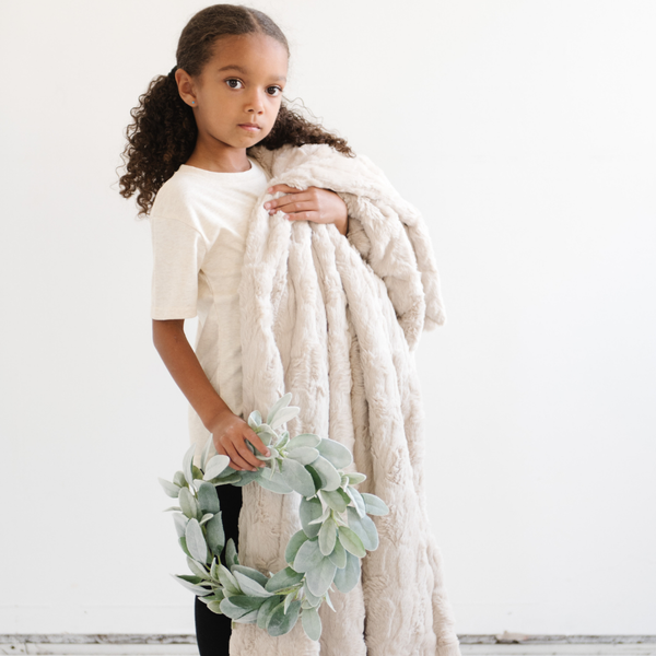 A little girl holds a light tan luxurious patterned faux fur throw blanket that is a Saranoni blanket. This ultra-soft, plush throw blanket adds a touch of elegance and warmth to any space, perfect as a soft throw blanket or fluffy blanket for lounging. Ideal for those seeking a high-quality artificial fur blanket or luxury blanket, this versatile and stylish soft blanket enhances both comfort and decor. Shop the best blankets and throws for ultimate relaxation and cozy vibes.