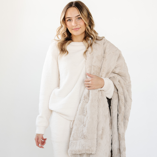 A woman holds a light tan luxurious patterned faux fur throw blanket that is a Saranoni blanket. This ultra-soft, plush throw blanket adds a touch of elegance and warmth to any space, perfect as a soft throw blanket or fluffy blanket for lounging. Ideal for those seeking a high-quality artificial fur blanket or luxury blanket, this versatile and stylish soft blanket enhances both comfort and decor. Shop the best blankets and throws for ultimate relaxation and cozy vibes.