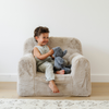 A happy boy sits on a cozy plush chair, joyfully holding a soft gray stuffed elephant. Dressed in a striped outfit, he beams with delight, showcasing the inviting texture of the chair and the comfort of his favorite toy. This charming scene highlights the perfect blend of stylish children's furniture and beloved stuffed animals, making it an ideal addition to any child's playroom or reading nook.