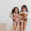 Two smiling girls sit side by side on a cozy white plush chair, each holding their stuffed animals—a pink bunny and a brown dog. Their joyful expressions capture the essence of childhood play and comfort, showcasing the perfect combination of stylish children's furniture and beloved plush toys. This delightful scene is ideal for parents searching for comfortable seating options and adorable toys for their children's play areas.