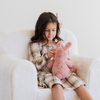 A young girl sits comfortably in a soft white plush chair, focused on her adorable pink stuffed bunny. Wearing a plaid dress and a lovely hair bow, she embodies the joy of playtime. This charming scene highlights the perfect combination of cozy children's furniture and cuddly plush toys, making it an ideal choice for parents searching for stylish seating and comforting companions for their kids.