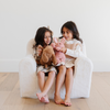 Two happy girls sit together on a cozy white plush chair, each holding their favorite stuffed animals—a brown dog and a pink bunny. Their joyful expressions and the soft textures of their toys highlight the importance of comfort and companionship in childhood. This delightful scene captures the essence of stylish children's furniture and cuddly plush toys, making it perfect for parents looking to create a warm and inviting play area for their kids.