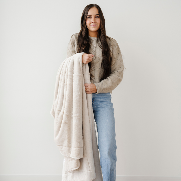 A woman holds a cream lush blanket that is an extra large blanket. This Saranoni blanket is also a luxury blanket and a soft blanket. Add to your home, gift to someone, or relax with this cozy blanket. Enjoy this luxury blanket for years to come. 