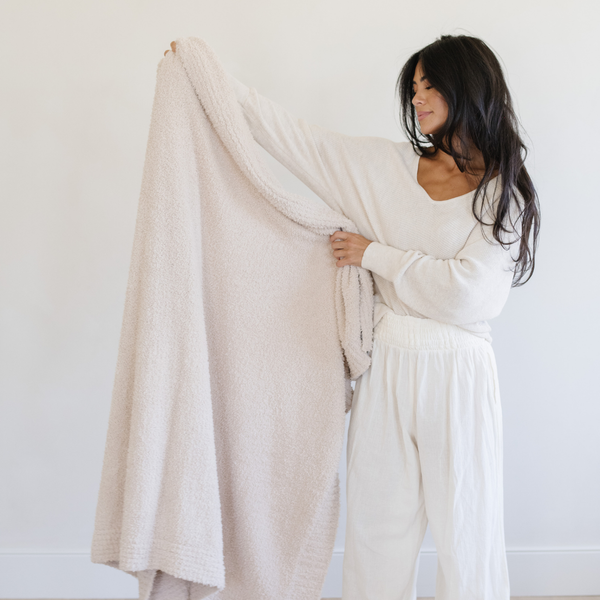 A woman holds a Bamboni® blanket by Saranoni. This ultra-soft blanket is a cream blanket and made from a premium blend of bamboo rayon and poly microfiber, offering a lightweight, breathable, and fluffy feel. Perfect as a extra large blanket, luxury blanket, or soft blanket, it adds warmth and elegance to any living room, bedroom, or home décor setting. Designed for ultimate comfort, this buttery-soft Saranoni blanket is ideal for gifting. Enjoy this cozy blanket for years to come!