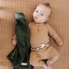 A baby boy holds a green lush blanket. The soft blanket is a baby blanket and a Saranoni blanket. He is laying on top of a white crib sheet with a camel colored stripes on the crib sheet. This crib sheet is a soft crib sheet and is a Saranoni crib sheet.