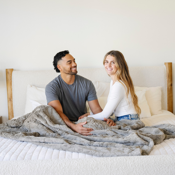 A husband and wife sit by a cashmere colored luxurious patterned faux fur extra large throw blanket that is a Saranoni blanket. This ultra-soft, cozy blanket adds a touch of elegance and warmth to any space, perfect as a soft oversized blanket or fluffy blanket for lounging. Ideal for those seeking a high-quality artificial fur blanket or luxury blanket, this versatile and stylish soft blanket enhances both comfort and decor. Shop the best blankets and throws for ultimate relaxation and cozy vibes.