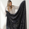A woman holds up a charcoal blanket that is an extra large blanket. This soft blanket is a lush blanket and also a Saranoni blanket. Use this luxury blanket for gifting, relaxing, or as an addition to your home decor. Enjoy this cozy blanket for years to come. 