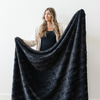 A woman holds up a charcoal luxurious patterned faux fur extra large throw blanket that is a Saranoni blanket. This ultra-soft, cozy blanket adds a touch of elegance and warmth to any space, perfect as a soft oversized blanket or fluffy blanket for lounging. Ideal for those seeking a high-quality artificial fur blanket or luxury blanket, this versatile and stylish soft blanket enhances both comfort and decor. Shop the best blankets and throws for ultimate relaxation and cozy vibes.