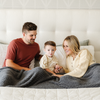 A husband, wife, and their little boy sit under a luxurious ribbed Bamboni® blanket by Saranoni, the blanket is a charcoal blanket. This ultra-soft blanket is crafted from bamboo rayon and poly microfiber, making it lightweight, breathable, and fluffy. Ideal as a cozy blanket, throw blanket, luxury blanket, soft blanket, or stylish home accent, this Saranoni blanket brings warmth, comfort, and timeless elegance to any living room or bedroom.