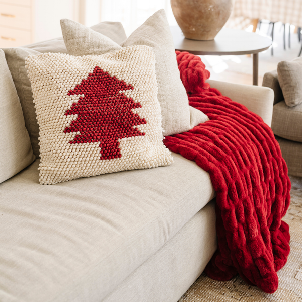 Plush red double ruched blanket draped over a neutral sofa with a festive red and white tree pillow, adding a pop of holiday color to the living room decor. The soft blanket is a luxury blanket and a Saranoni blanket. 