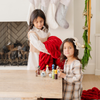 Two young girls near a fireplace with a vibrant red double ruched blanket and Christmas decorations in the background. Perfect for creating cozy, holiday-themed spaces. The soft blanket is a luxury blanket and a Saranoni blanket. 