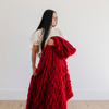 Woman showcasing a luxurious red double ruched blanket, highlighting its soft, textured design. Ideal for winter decor and holiday-themed home styling. The soft blanket is a luxury blanket and a Saranoni blanket. 