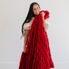 Woman showcasing a luxurious red double ruched blanket, highlighting its soft, textured design. Ideal for winter decor and holiday-themed home styling. The soft blanket is a luxury blanket and a Saranoni blanket. 