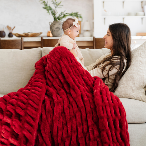 Mother and baby sharing a cozy moment on the sofa with a plush red double ruched blanket, adding warmth and holiday spirit to the room. Ideal for festive decor and family relaxation. The soft blanket is a luxury blanket and a Saranoni blanket.