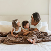 A mother and her son and daughter sit with a brown luxurious patterned faux fur extra large throw blanket that is a Saranoni blanket. This ultra-soft, cozy blanket adds a touch of elegance and warmth to any space, perfect as a soft oversized blanket or fluffy blanket for lounging. Ideal for those seeking a high-quality artificial fur blanket or luxury blanket, this versatile and stylish soft blanket enhances both comfort and decor. Shop the best blankets and throws for ultimate relaxation and cozy vibes.