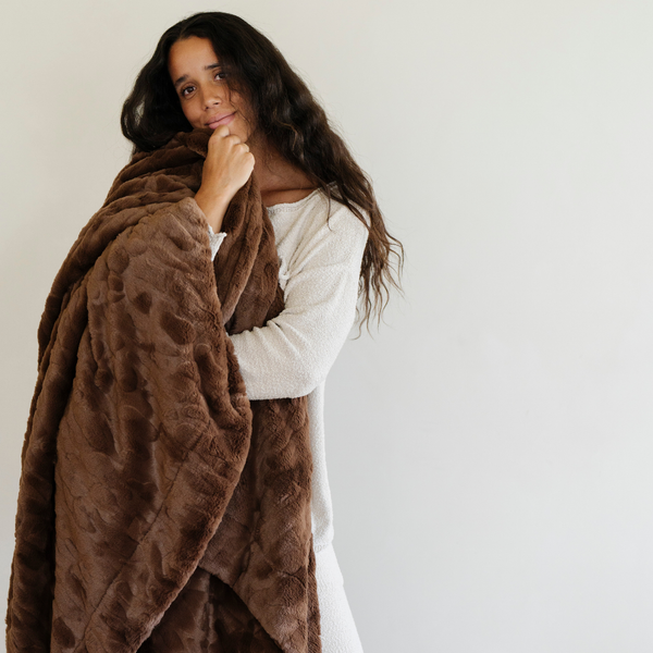 A woman holds a brown luxurious patterned faux fur extra large throw blanket that is a Saranoni blanket. This ultra-soft, cozy blanket adds a touch of elegance and warmth to any space, perfect as a soft oversized blanket or fluffy blanket for lounging. Ideal for those seeking a high-quality artificial fur blanket or luxury blanket, this versatile and stylish soft blanket enhances both comfort and decor. Shop the best blankets and throws for ultimate relaxation and cozy vibes.