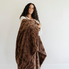 A woman smiles and holds a brown luxurious patterned faux fur extra large throw blanket that is a Saranoni blanket. This ultra-soft, cozy blanket adds a touch of elegance and warmth to any space, perfect as a soft oversized blanket or fluffy blanket for lounging. Ideal for those seeking a high-quality artificial fur blanket or luxury blanket, this versatile and stylish soft blanket enhances both comfort and decor. Shop the best blankets and throws for ultimate relaxation and cozy vibes.