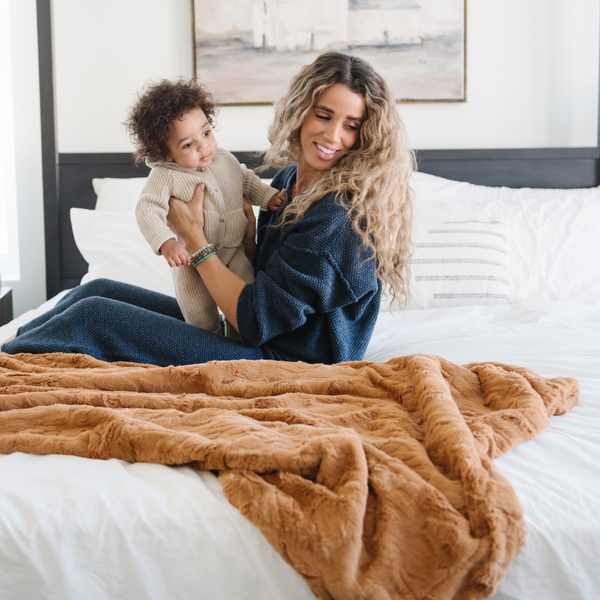 A mother and her little boy sit by a copper colored luxurious patterned faux fur throw blanket that is a Saranoni blanket. This ultra-soft, plush throw blanket adds a touch of elegance and warmth to any space, perfect as a soft throw blanket or fluffy blanket for lounging. Ideal for those seeking a high-quality artificial fur blanket or luxury blanket, this versatile and stylish soft blanket enhances both comfort and decor. Shop the best blankets and throws for ultimate relaxation and cozy vibes.